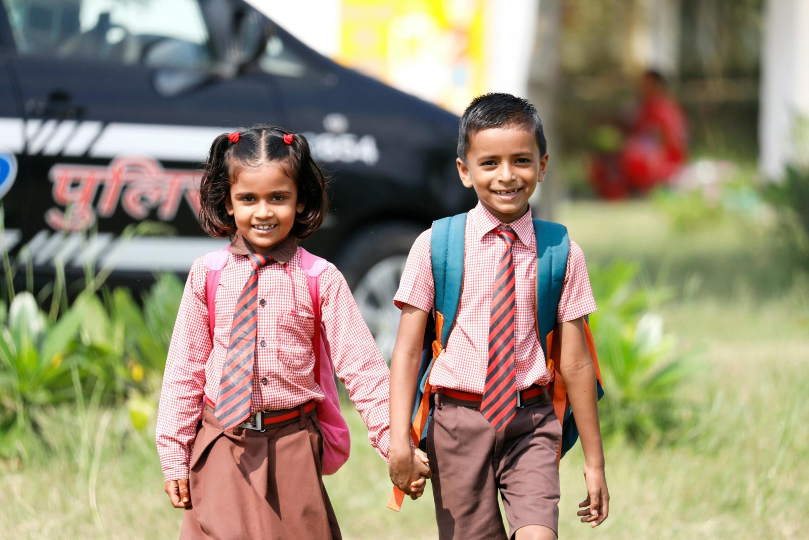 Two cheerful school children in uniforms holding hands and walking outdoors.